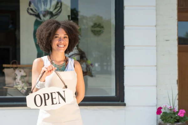 how to choose seo keywords for small business An entrepreneur wearing an apron smiles while holding an "open" sign as she stands in front of her small business