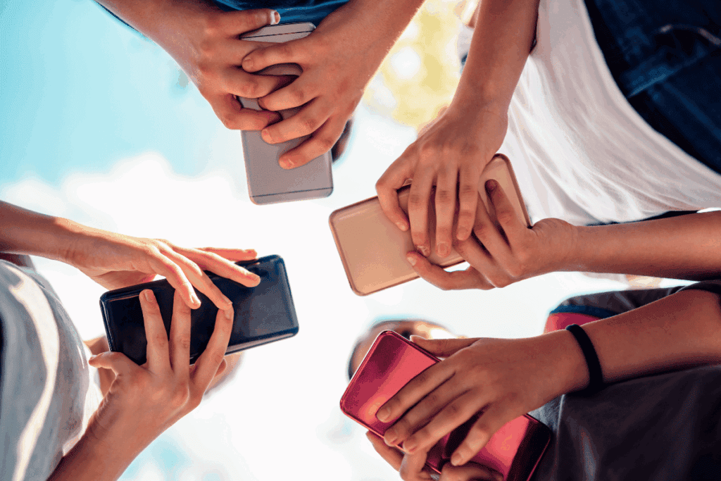 Looking up at the hands of four people visiting websites on smartphones outdoors with clouds floating above