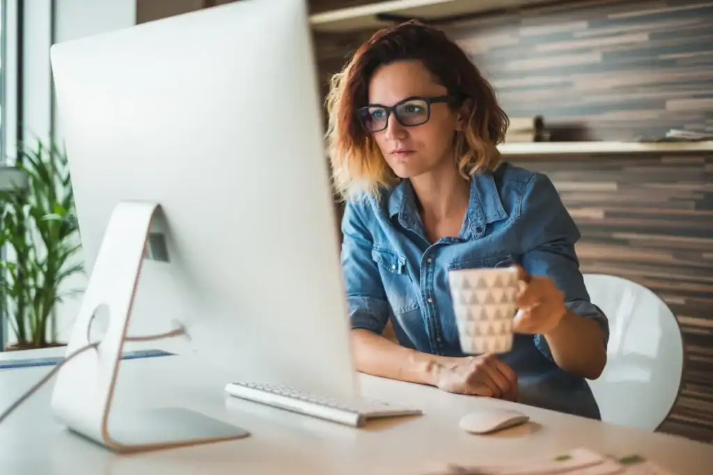 An entrepreneur looks at the business systems working together on her computer monitor while holding a cup of coffee