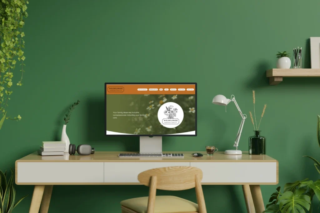 a computer sits on a desk surrounded by plants. The monitor shows a custom website designed by Nikki Shaheed