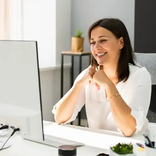 a small business owner smiles at her computer, pleased with her systems that are working together seamlessly