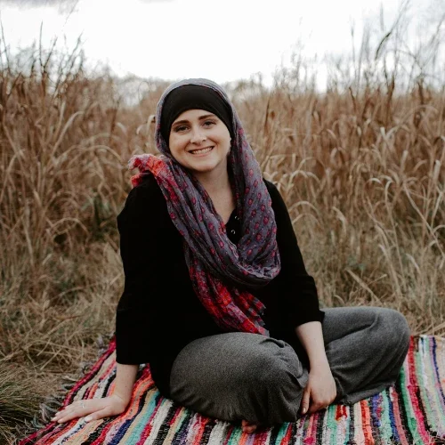 Web designer Nikki Shaheed sits on a colorful rug in a grassy field